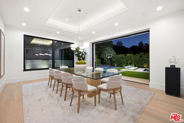 dining area with light wood-type flooring and a raised ceiling