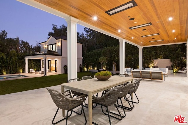 patio terrace at dusk featuring outdoor lounge area, a balcony, and a swimming pool