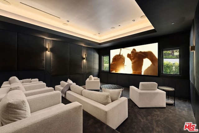 cinema room with a raised ceiling, a healthy amount of sunlight, and dark colored carpet