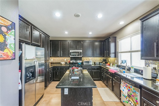 kitchen featuring a kitchen island, light hardwood / wood-style flooring, appliances with stainless steel finishes, dark stone countertops, and decorative backsplash