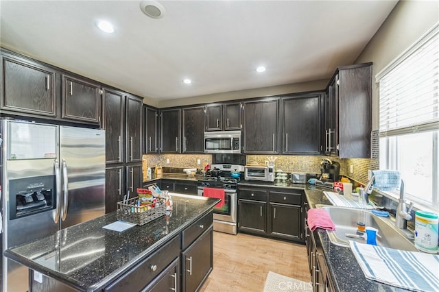 kitchen with dark brown cabinets, appliances with stainless steel finishes, light hardwood / wood-style floors, and dark stone counters