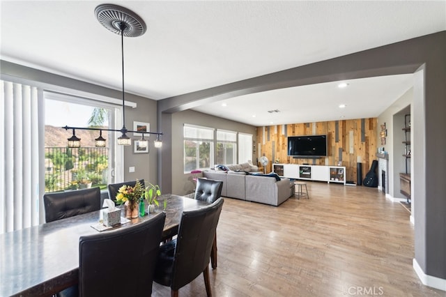 dining area with light hardwood / wood-style flooring, wood walls, and a healthy amount of sunlight