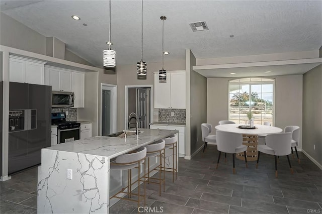 kitchen featuring tasteful backsplash, appliances with stainless steel finishes, an island with sink, and white cabinetry