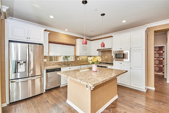 kitchen featuring appliances with stainless steel finishes, light wood-type flooring, a kitchen island, decorative light fixtures, and white cabinetry