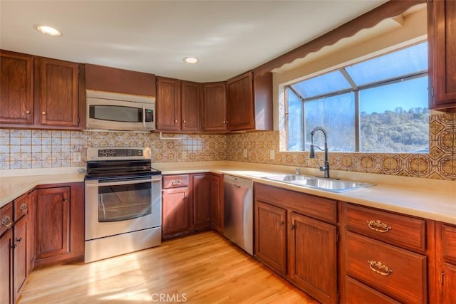 kitchen with light wood-style flooring, stainless steel appliances, a sink, light countertops, and tasteful backsplash