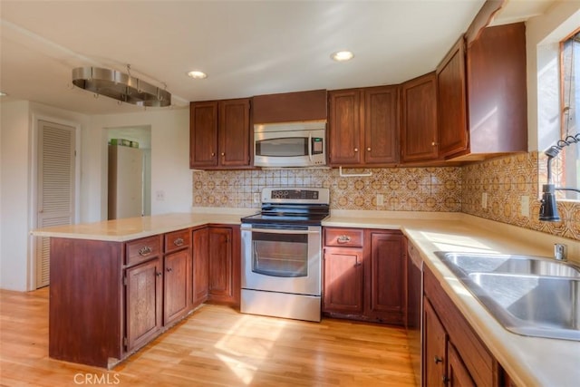 kitchen with light wood finished floors, a peninsula, stainless steel appliances, light countertops, and a sink