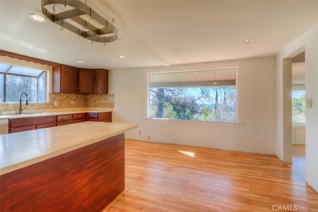 kitchen featuring light countertops, decorative backsplash, brown cabinetry, light wood-style floors, and a sink