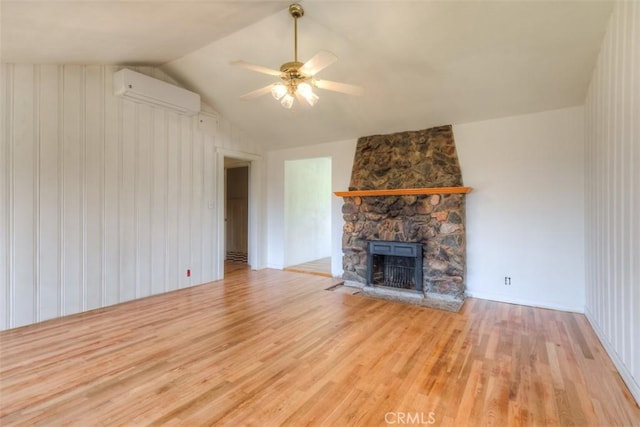 unfurnished living room featuring vaulted ceiling, wood finished floors, a wall unit AC, and a fireplace