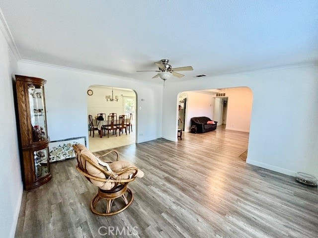 living room with crown molding, wood-type flooring, and ceiling fan with notable chandelier