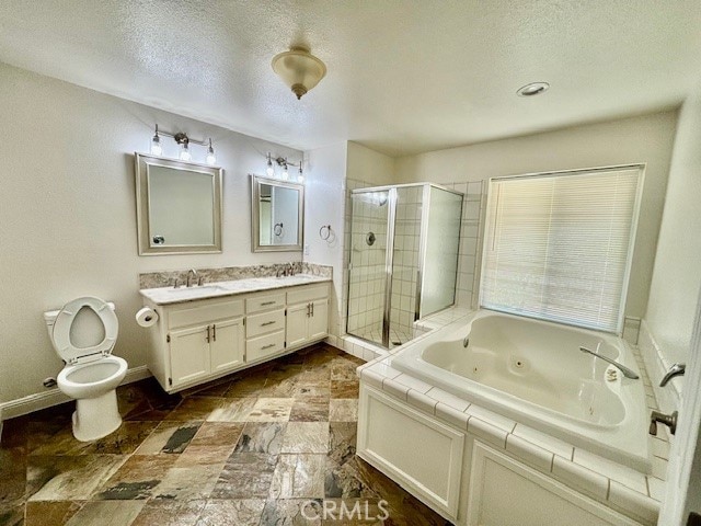 full bathroom with a textured ceiling, toilet, vanity, and separate shower and tub