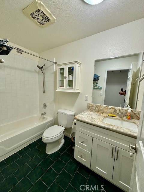 full bathroom with tiled shower / bath, vanity, a textured ceiling, tile patterned floors, and toilet