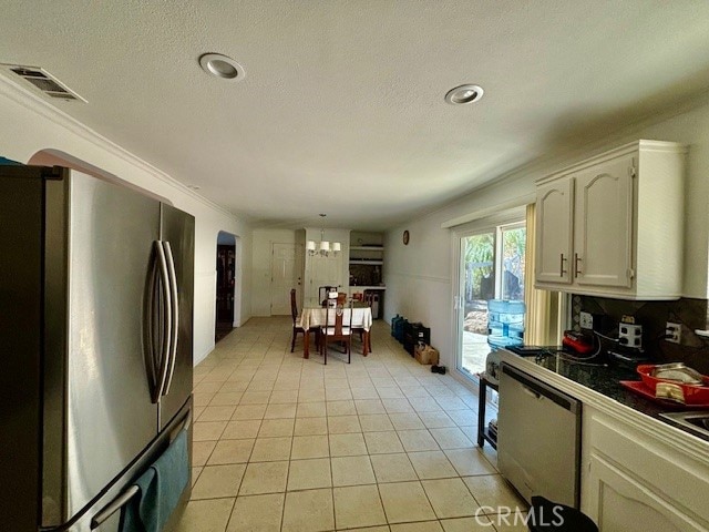 kitchen with a notable chandelier, white cabinetry, stainless steel appliances, light tile patterned floors, and crown molding