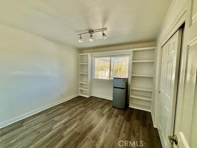 interior space featuring a textured ceiling, rail lighting, stainless steel refrigerator, a closet, and dark hardwood / wood-style floors