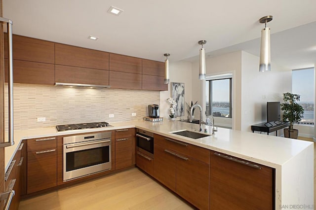 kitchen featuring sink, decorative light fixtures, kitchen peninsula, black gas cooktop, and oven