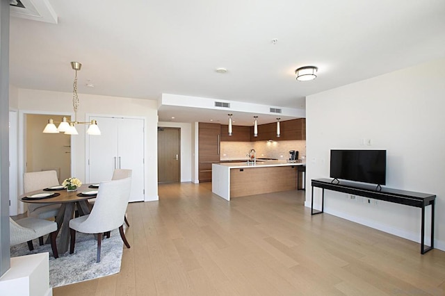 kitchen featuring sink, tasteful backsplash, decorative light fixtures, a center island with sink, and light hardwood / wood-style floors