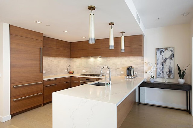 kitchen featuring sink, tasteful backsplash, decorative light fixtures, kitchen peninsula, and light hardwood / wood-style floors