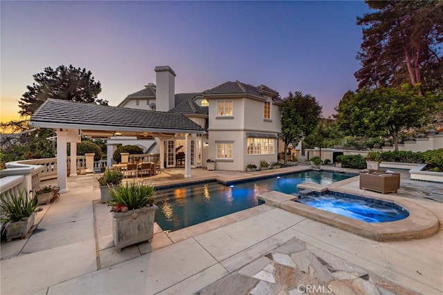 pool at dusk featuring an in ground hot tub and a patio area