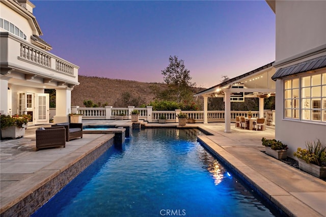 pool at dusk featuring an in ground hot tub and a patio area