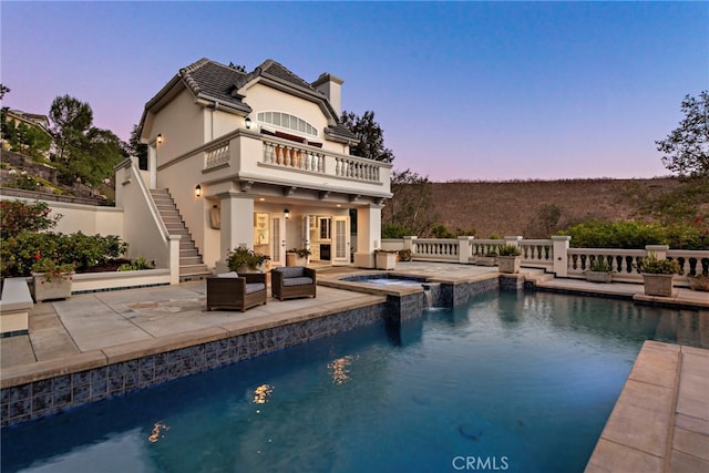 back house at dusk with a pool with hot tub, a balcony, and a patio