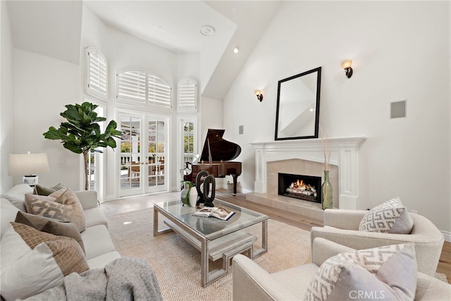 living room featuring a tile fireplace, french doors, a towering ceiling, and light wood-type flooring