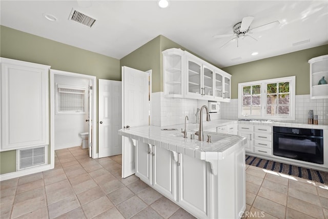 kitchen featuring white cabinets, tile counters, light tile patterned floors, black oven, and kitchen peninsula