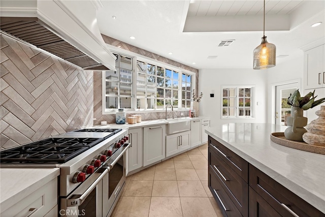 kitchen featuring sink, premium range hood, designer stove, decorative light fixtures, and white cabinets