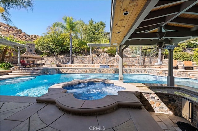 view of pool featuring an in ground hot tub, an outdoor stone fireplace, pool water feature, a mountain view, and a patio