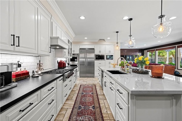 kitchen featuring sink, built in appliances, a large island with sink, pendant lighting, and white cabinets