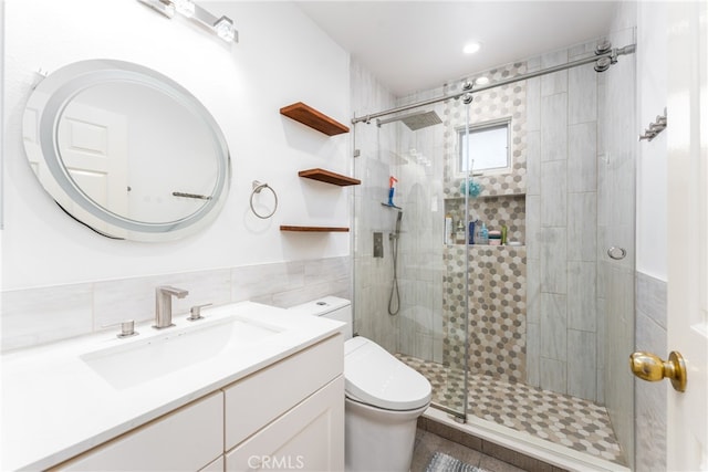 bathroom featuring tile walls, vanity, a shower with shower door, and toilet