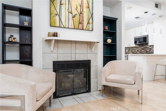 living room featuring built in shelves, light wood-type flooring, and a tiled fireplace