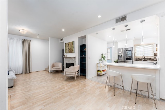 kitchen with a kitchen breakfast bar, hanging light fixtures, white cabinetry, light hardwood / wood-style flooring, and stainless steel refrigerator with ice dispenser