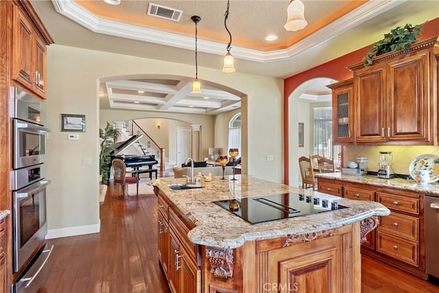 kitchen with pendant lighting, coffered ceiling, a kitchen island with sink, stainless steel appliances, and dark wood-type flooring