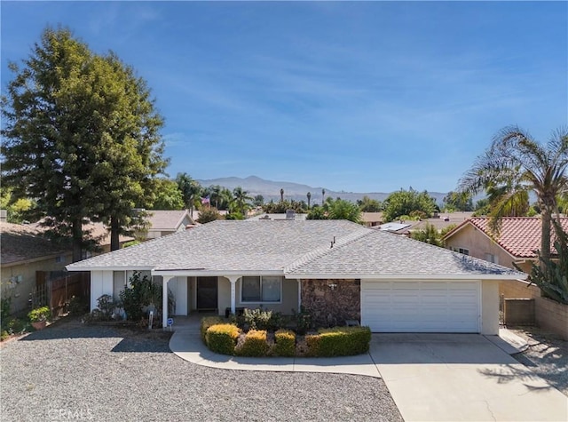 ranch-style home featuring fence, concrete driveway, an attached garage, roof with shingles, and a mountain view
