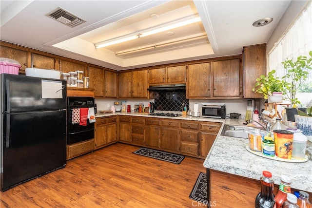 kitchen with light wood-type flooring, a raised ceiling, sink, and black appliances