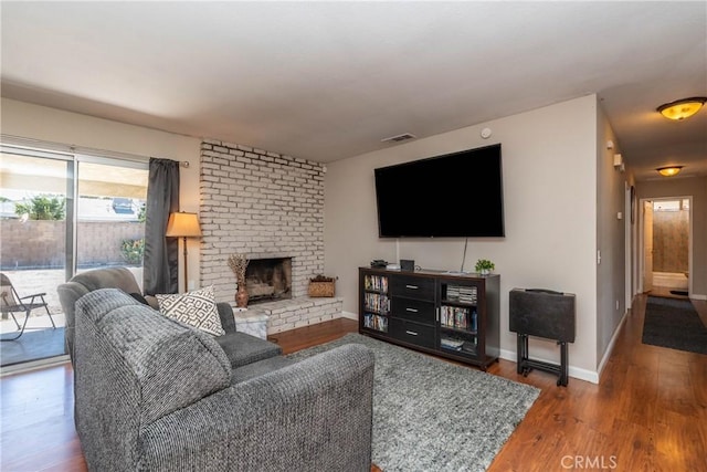 living room with baseboards, a brick fireplace, wood finished floors, and visible vents