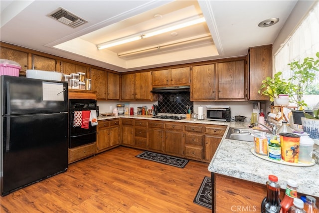 kitchen featuring light hardwood / wood-style flooring, black appliances, a tray ceiling, and sink