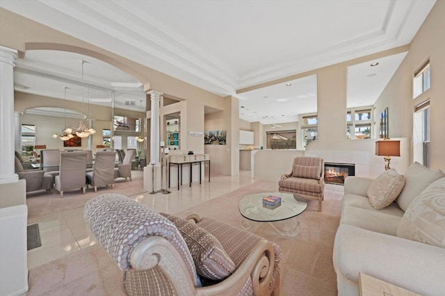 living room featuring decorative columns, light tile patterned flooring, a tiled fireplace, and a tray ceiling