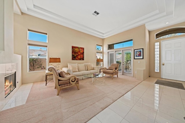 tiled living room featuring a raised ceiling, a fireplace, and a high ceiling