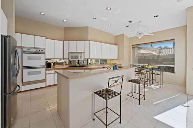 kitchen with a kitchen bar, stainless steel appliances, ceiling fan, light tile patterned floors, and white cabinetry