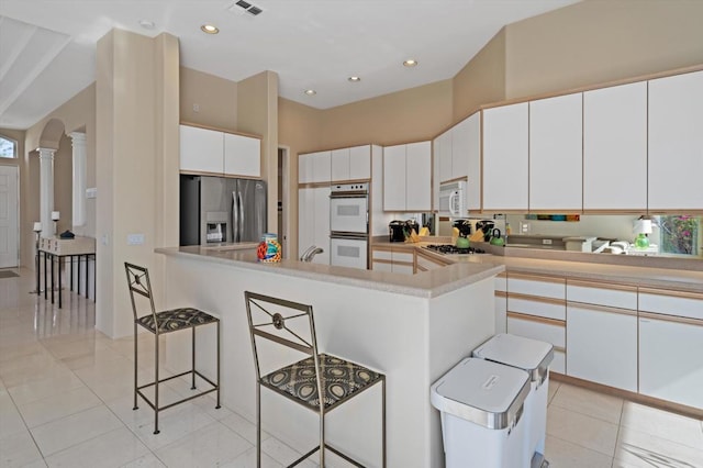 kitchen with white cabinetry, stainless steel appliances, decorative columns, a kitchen bar, and a kitchen island