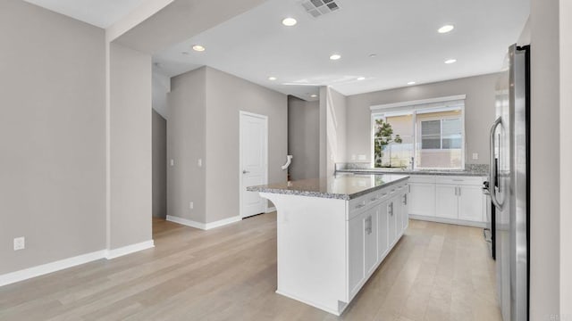 kitchen featuring stainless steel refrigerator, white cabinetry, a center island, light stone counters, and light hardwood / wood-style flooring