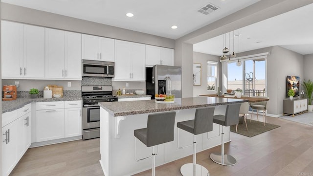 kitchen with light stone countertops, stainless steel appliances, light hardwood / wood-style flooring, and a kitchen island