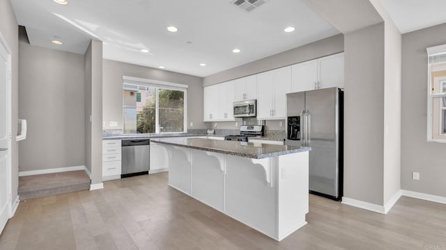 kitchen with dark stone counters, a kitchen breakfast bar, a kitchen island, white cabinetry, and stainless steel appliances