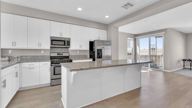 kitchen featuring a center island, light stone countertops, stainless steel appliances, and white cabinetry