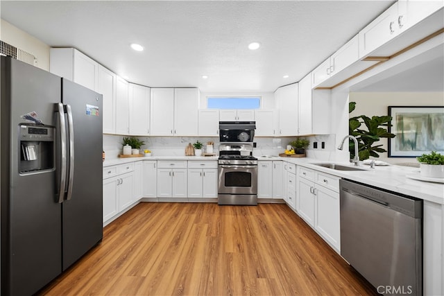 kitchen with appliances with stainless steel finishes, a textured ceiling, sink, light hardwood / wood-style floors, and white cabinetry