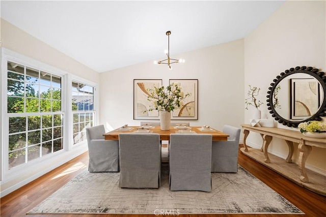 dining space with hardwood / wood-style floors, lofted ceiling, and a notable chandelier