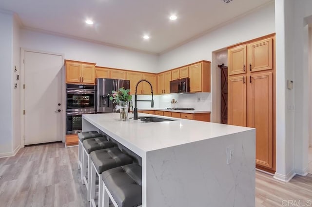 kitchen featuring sink, a kitchen breakfast bar, light hardwood / wood-style flooring, a center island with sink, and appliances with stainless steel finishes