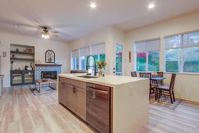 kitchen featuring a tile fireplace, ceiling fan, sink, an island with sink, and light hardwood / wood-style floors