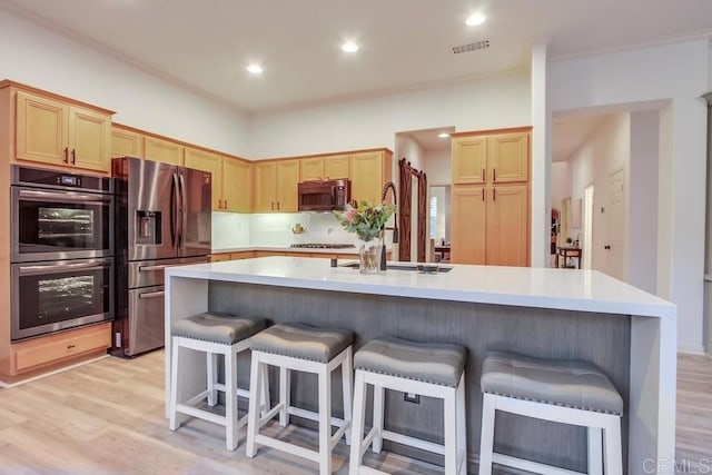 kitchen featuring appliances with stainless steel finishes, light wood-type flooring, light brown cabinetry, a breakfast bar, and a kitchen island with sink