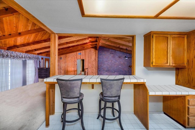 kitchen with a kitchen bar, kitchen peninsula, tile counters, and lofted ceiling with beams